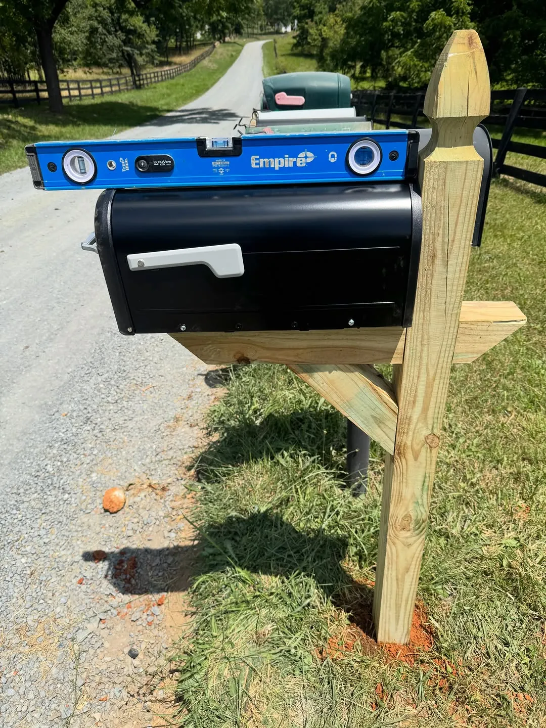 Two mailboxes on a newly set wooden post beside a rural fence line