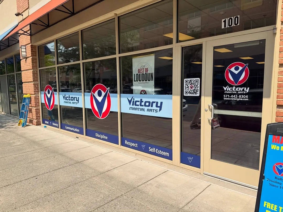 Storefront windows wrapped in blue and red Victory Martial Arts graphics with door decals