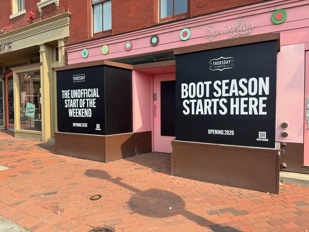 Black seasonal window graphics reading Boot Season Starts Here across a pink retail storefront