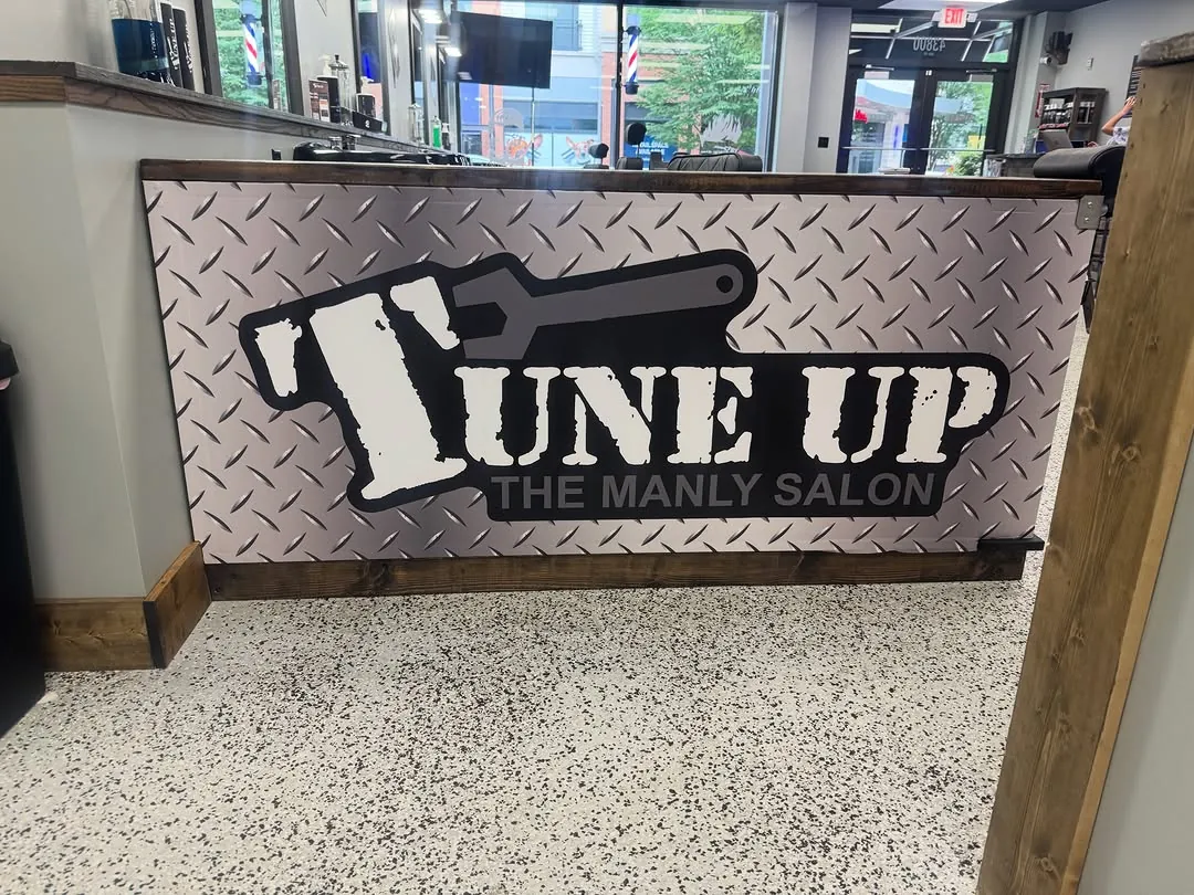 Diamond-plate exterior sign reading Tune Up The Manly Salon mounted on a post