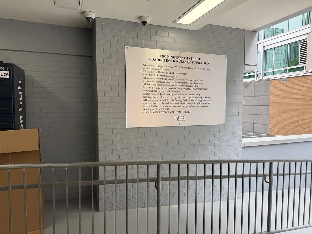 Engraved building plaque installed on an exterior concrete wall beside a stair rail