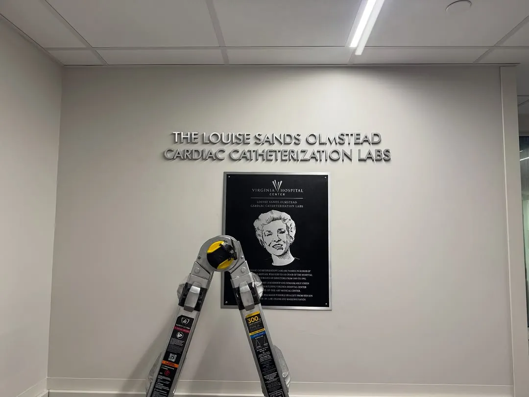 Dimensional letters and a dedication plaque installed above a ladder in a hospital corridor